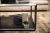 Eine elegante, moderne Wohnzimmereinrichtung mit einem Couchtisch aus schwarzem Glas, auf dem eine minimalistische Vase und eine kleine Sukkulente stehen, im Kontrast zu den weichen Texturen eines neutralen Sofas und Teppichs, die auf der 201 vorgestellt wurden