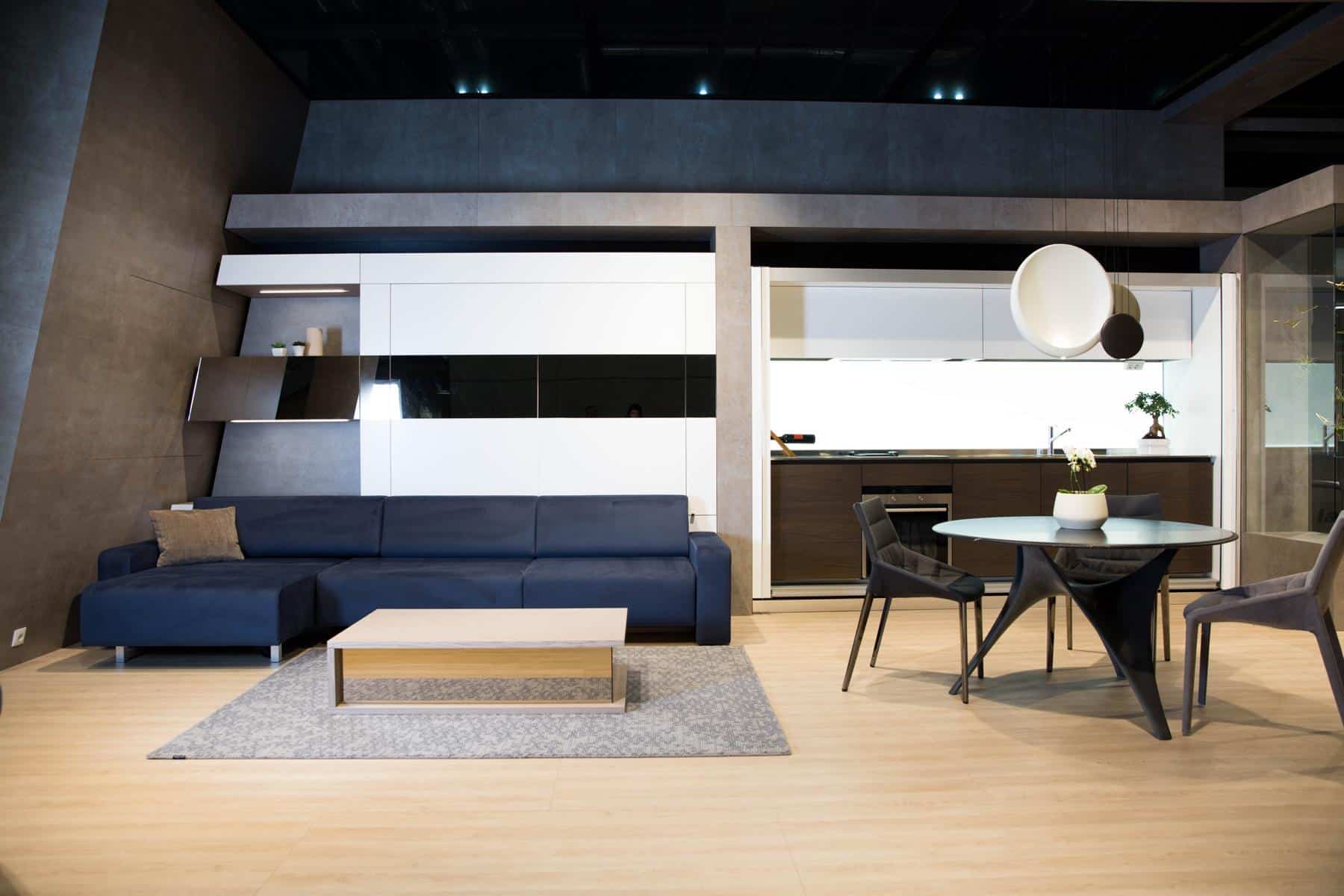 Ein modernes Wohnzimmer mit eleganten Möbeln und modernem Design, einem marineblauen Sofa, einem Couchtisch aus Holz und Glas und einer offenen Küche im Hintergrund, die auf der Messe 2016 vorgestellt wurde
