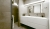Modernes Badezimmer mit einem eleganten weißen Waschtisch mit integriertem Waschbecken, großem Spiegel mit LED-Beleuchtung und grauen strukturierten Wänden in einem Wiener Mikroapartment, das eine minimalistische und zeitgenössische Ästhetik ausstrahlt.