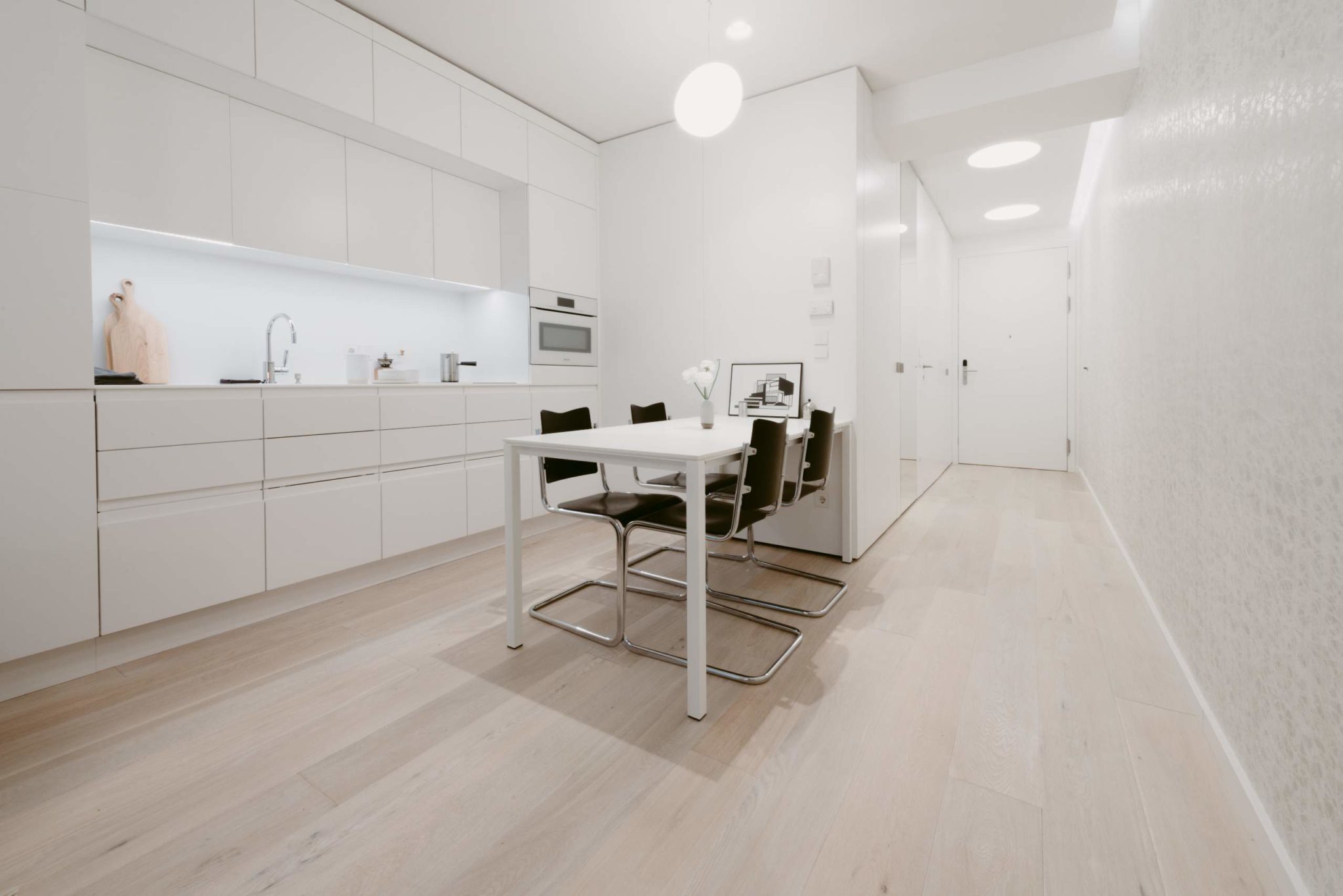 Eine elegante, moderne Küche mit weißen Schränken und einem Esstisch vor einem minimalistischen Innendesign, ideal für Wiens Mikroapartments.