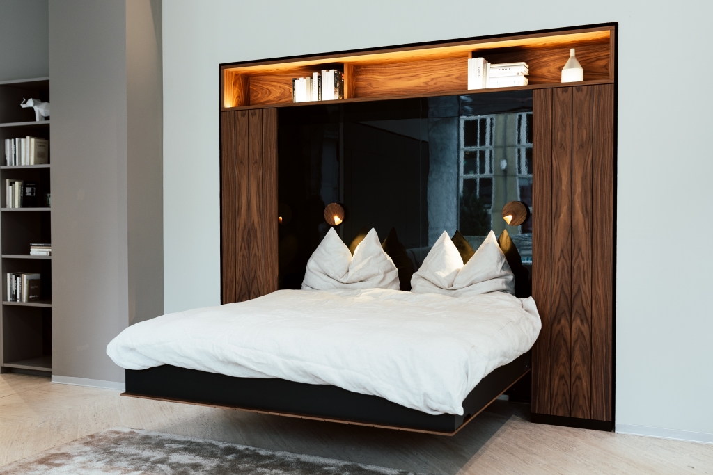 Ein modernes Schlafzimmer mit einem großen Bett mit weißer Bettwäsche und goldenen Kissen, flankiert von eingebauten Holzregalen und eleganten Wandlampen, die einen gemütlichen und dennoch luxuriösen Schlafraum schaffen.
