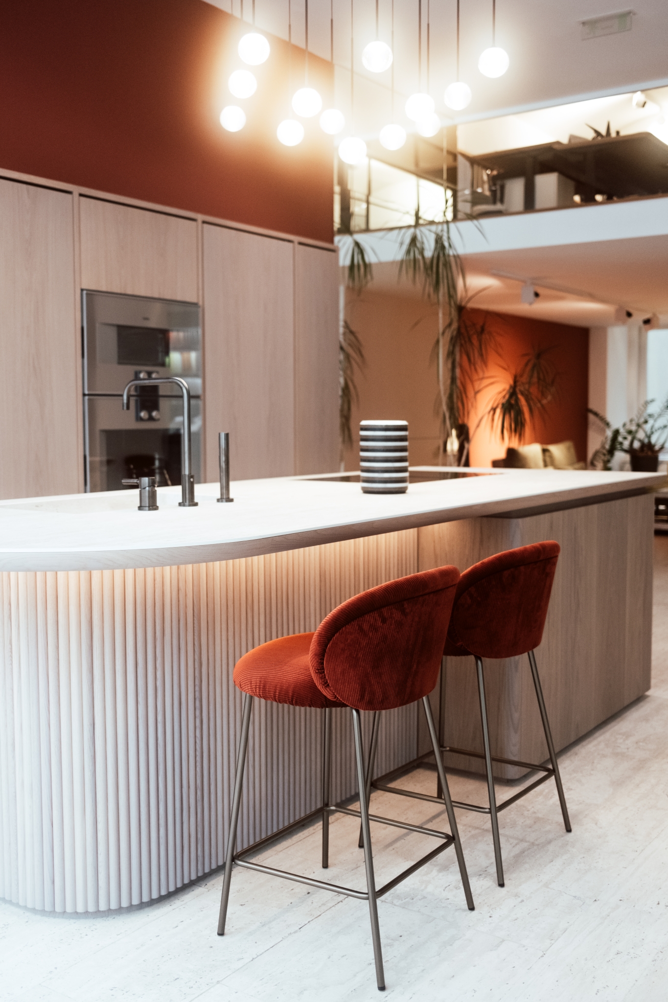 Moderne Kücheneinrichtung mit einer eleganten Kücheninsel, Pendelleuchten und stilvollen roten Barhockern.