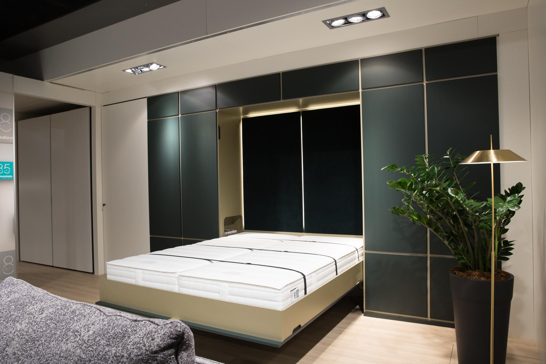 Moderne Schlafzimmereinrichtung mit einem großen Bett und Schiebetüren zum Kleiderschrank sowie einer gemütlichen Atmosphäre, die durch warmes Licht und eine Topfpflanze betont wird.