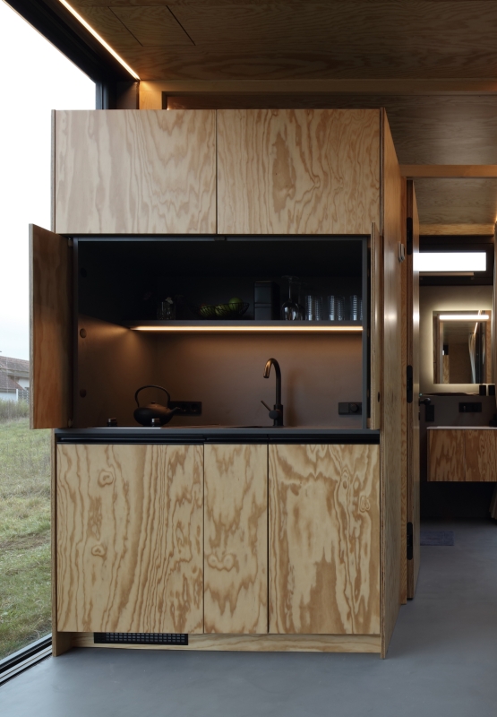 Moderne, kompakte Küche mit Holzschränken und eleganten schwarzen Arbeitsplatten, nahtlos integriert in den minimalistischen Wohnraum eines Tinyhouses.