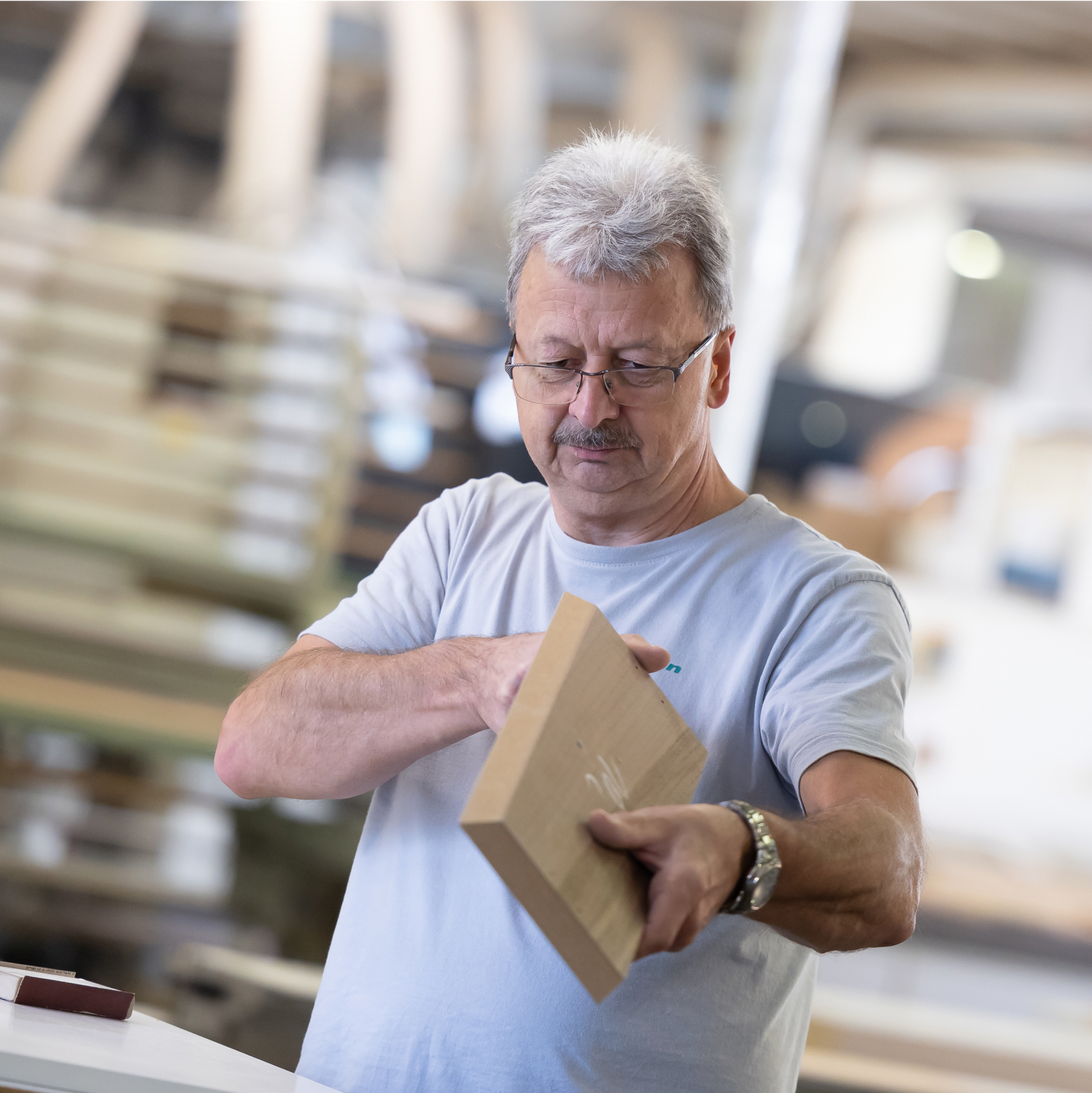 Handwerker inspiziert einen Holzblock mit Fokus und Fachwissen in einer Werkstattumgebung.